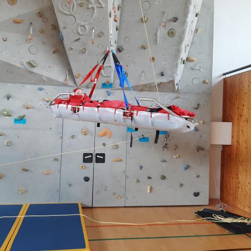 Bergrettung in der Turnhalle: ein Schüler wird mit einer Trage bei der Kletterwand geborgen